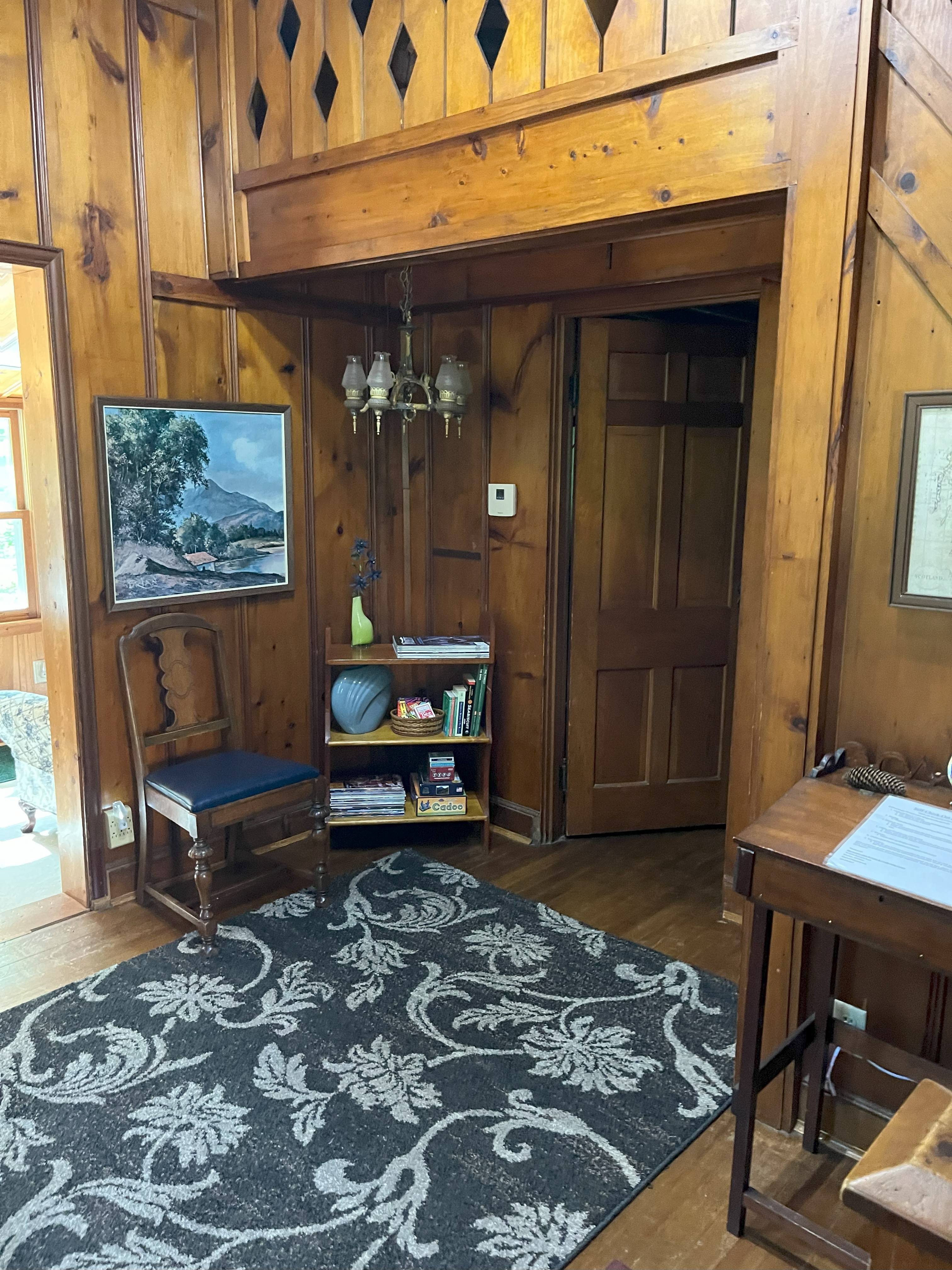 First floor sitting area with knotty pine walls, bookshelf, and period furnishings